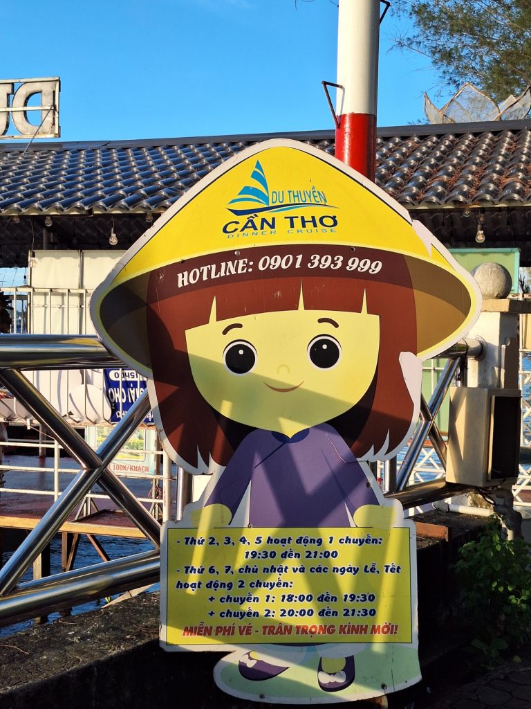 Biển hiệu hình cô gái mặc áo bà ba giới thiệu lịch trình hoạt động và số hotline của Du thuyền Bến Ninh Kiều Cần Thơ .