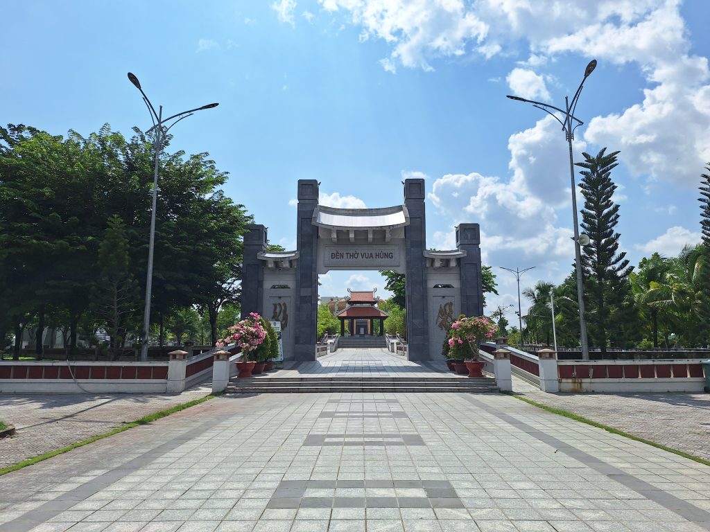 Cổng chính Đền thờ Vua Hùng Cần Thơ bằng đá xám hiện đại, phía trên khắc dòng chữ "ĐỀN THỜ VUA HÙNG", mở lối nhìn thẳng vào nhà bia bên trong dưới trời xanh.
