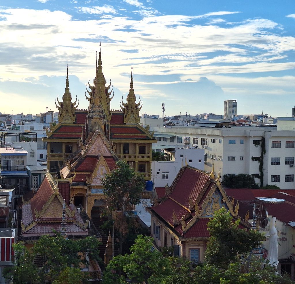 Góc chụp từ trên cao xuống khuôn viên ngôi chùa Khmer Munir Ansay độc đáo tại Cần Thơ, làm nổi bật những mái tháp nhọn màu vàng rực rỡ mang đậm nét kiến trúc Angkor truyền thống, bao quanh là rặng cây xanh và các tòa nhà đô thị.