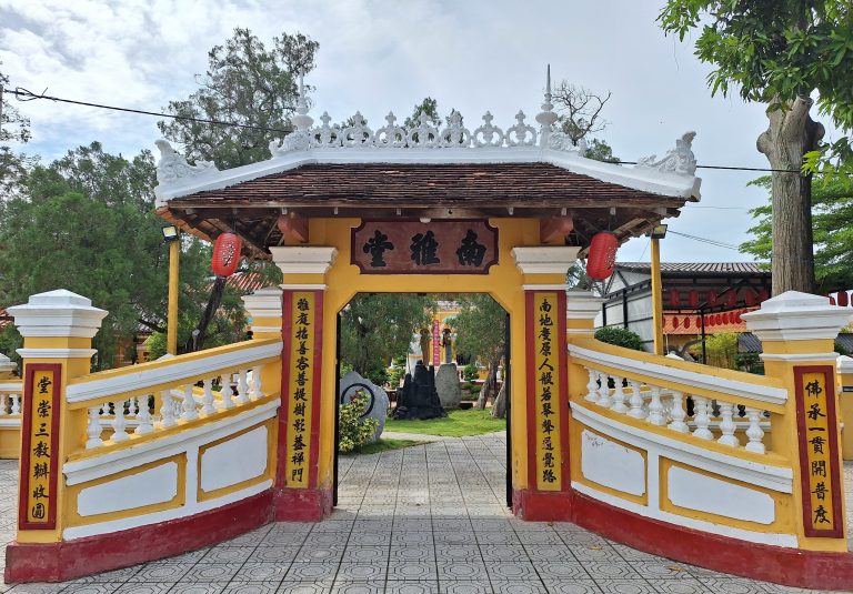 Cổng tam quan chính diện lối vào Chùa Nam Nhã với biển hiệu gỗ khắc chữ Hán "Nam Nhã Đường", thành cổng uốn cong sơn màu vàng đỏ, hai bên cột có câu đối và trên mái lợp ngói đen treo lồng đèn đỏ.