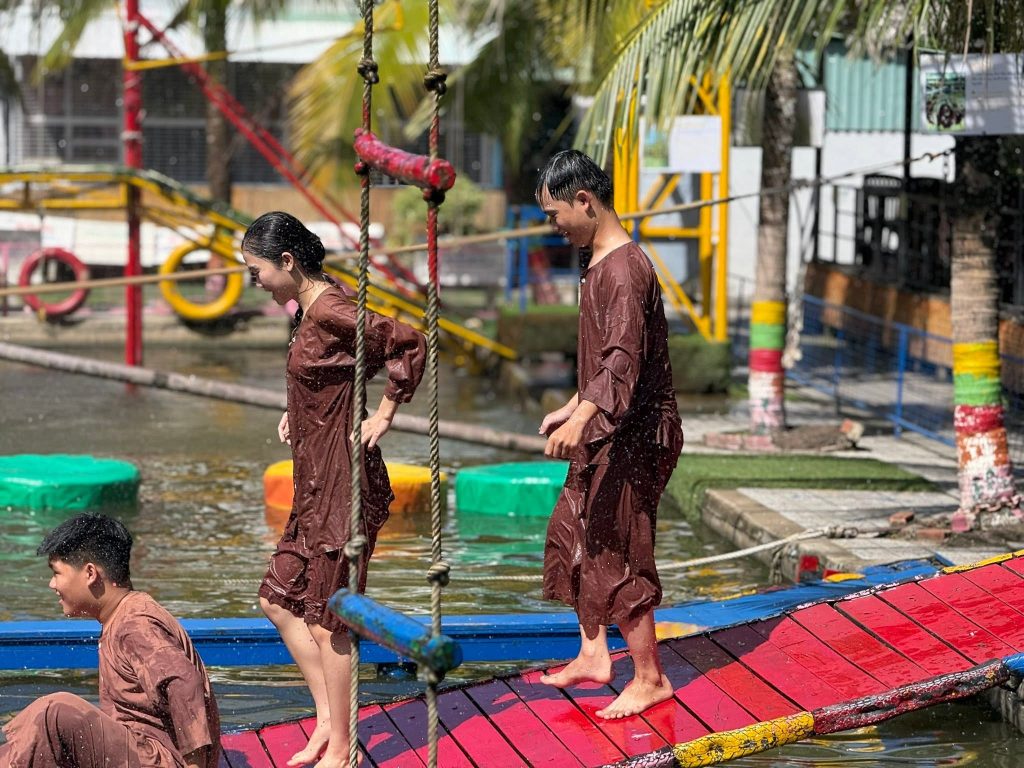 Du khách mặc áo bà ba truyền thống tham gia trò chơi đi cầu lắc dân gian vui nhộn tại Làng du lịch sinh thái Ông Đề Cần Thơ.