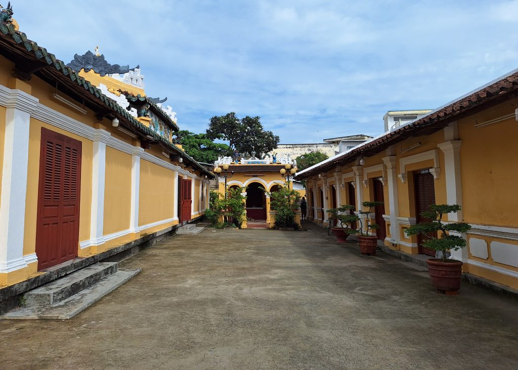 Lối đi tráng xi măng chạy dọc giữa các dãy nhà tường sơn vàng, cửa gỗ đỏ và các chậu cây kiểng bonsai của Đình Bình Thủy.