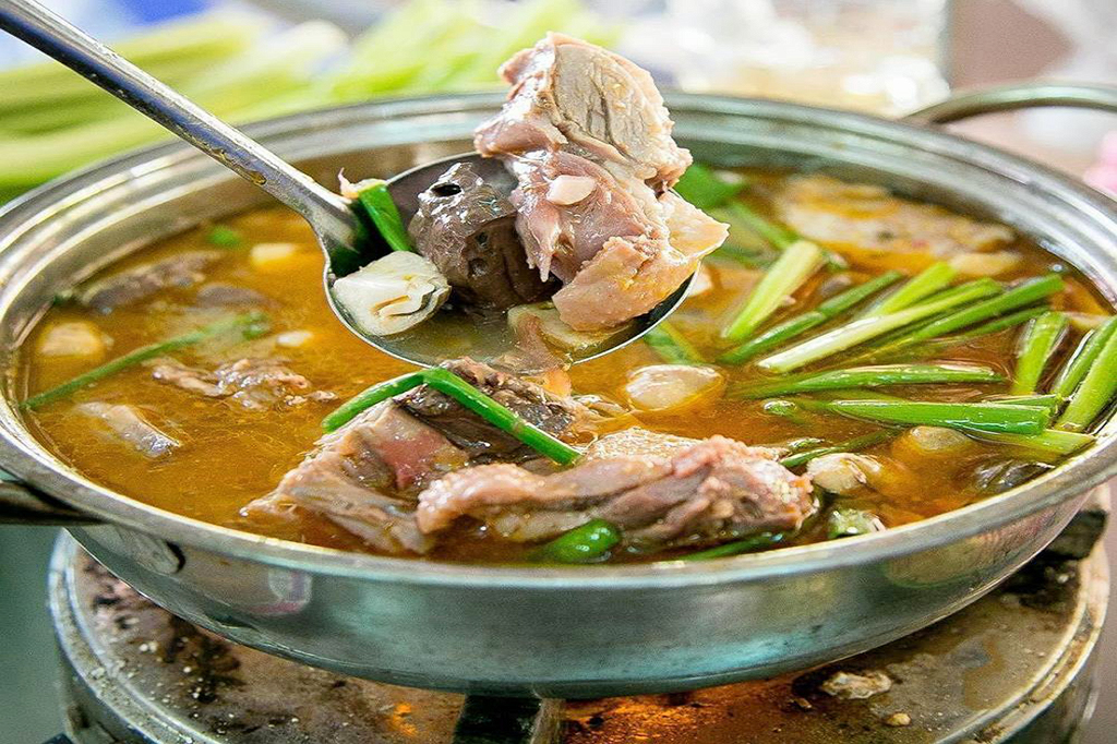 Cận cảnh một chiếc muôi đang múc thịt vịt và huyết từ nồi lẩu vịt nấu chao đặc sản Cần Thơ thơm ngon, nước lẩu sóng sánh đậm đà với nhiều hành lá.